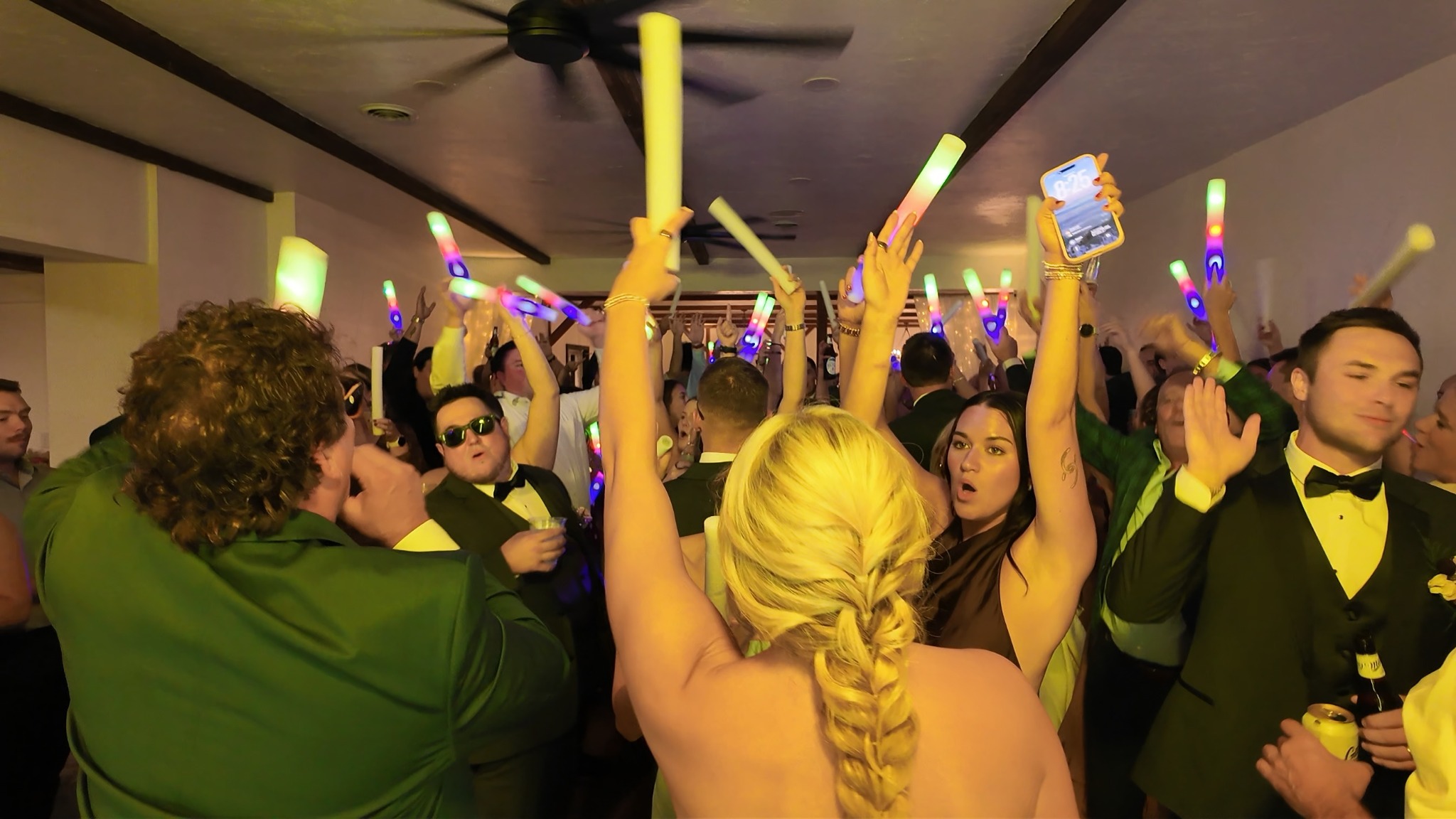 Packed wedding dance floor with guests celebrating and holding colorful LED foam sticks